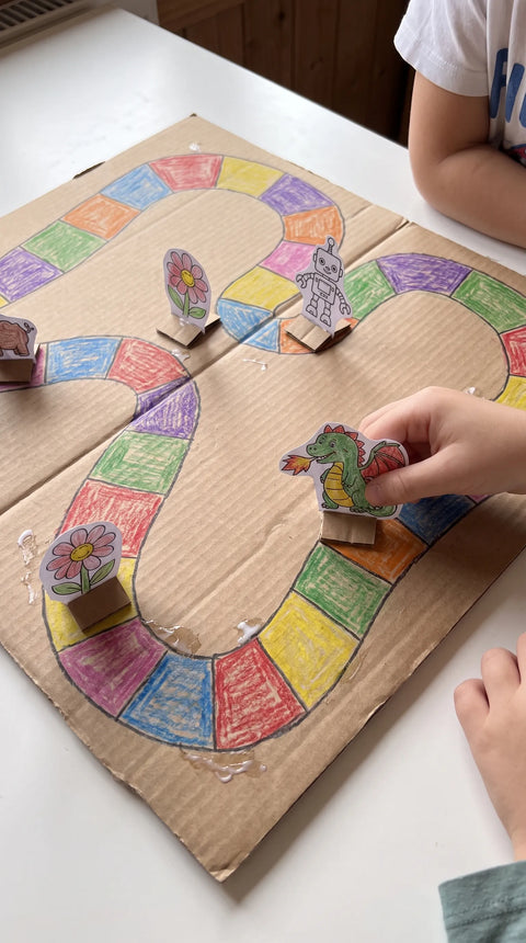 Kinder gestalten ein buntes Brettspiel aus Karton mit kleinen ausgeschnittenen Papierfiguren.