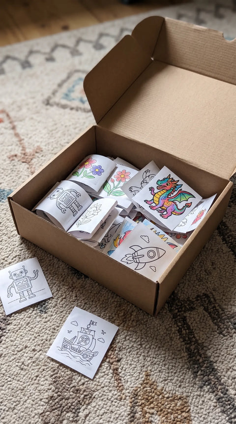 Eine offene Schachtel sammelt kleine schwarzweiße und bunt gestaltete Papiermotive.