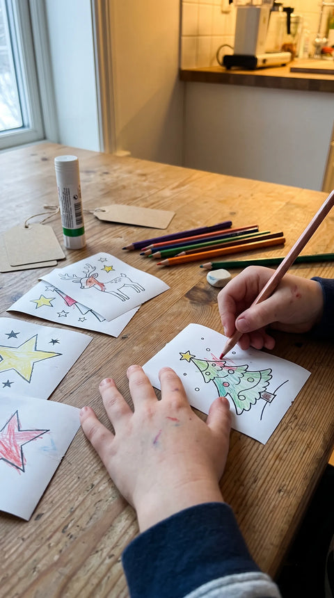 Kinderhände malen kleine Weihnachtsmotive mit Buntstiften aus.